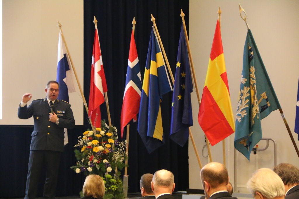 Generalmajor Michael Claesson från Sverige framför nordiska flaggor, EU-flaggan och en briggadflagga.